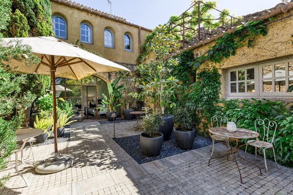 A courtyard with potted plants, a table with chairs, and a pergola with an umbrella.