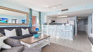 A compact living space with a sofa, coffee table, and a kitchenette area. - Bay Watch 509 (North Myrtle Beach)