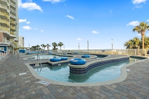 A swimming pool area with multiple water slides, a brick walkway, and a palm tree in the background.