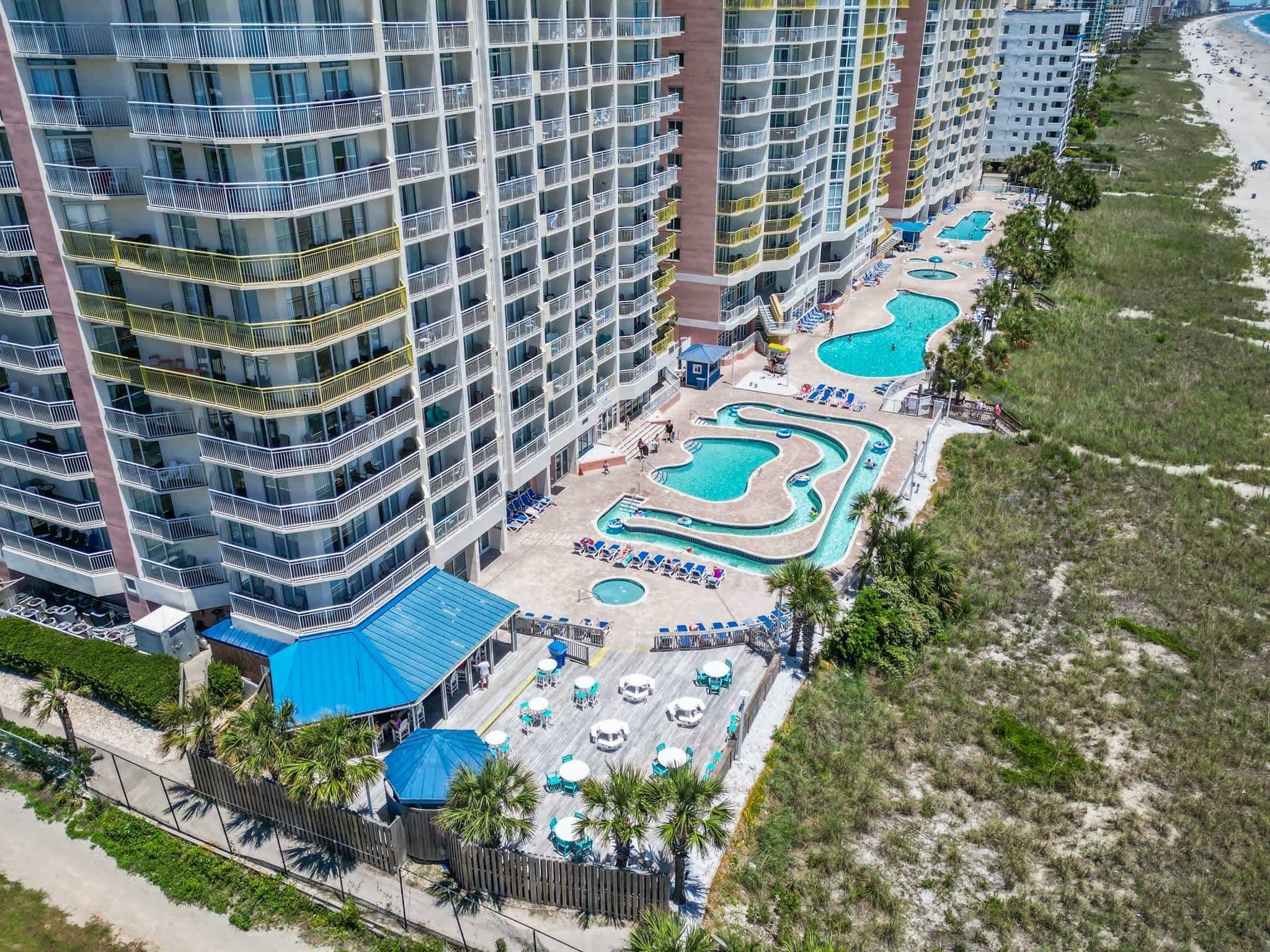 A high-rise hotel with multiple balconies, a pool area with lounge chairs, and a beach view.