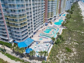 Un hĂŽtel de grande hauteur dotĂ© de nombreux balcons, dâun espace piscine avec des chaises longues et offrant une vue sur la plage.