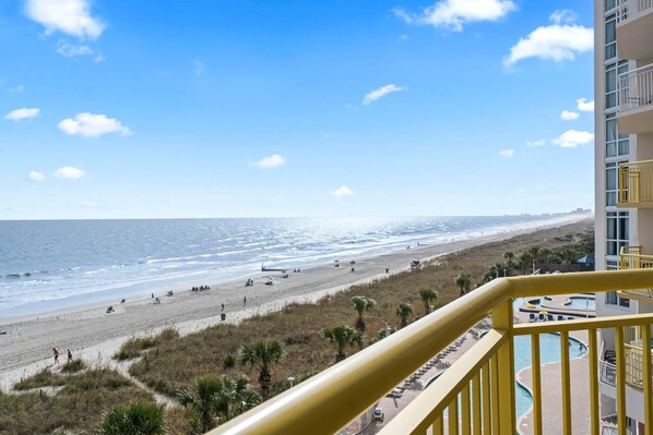 A beachfront view from a balcony with a pool and a beach in the background.