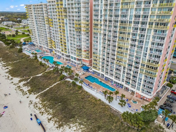 A high-rise hotel with multiple balconies, a pool area, and a beach view.