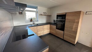 A modern kitchen with a black countertop, wooden cabinets, a built-in oven, and a window with a view of greenery.