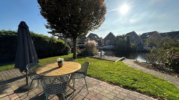 Une terrasse avec une table ronde en bois et des chaises, une petite plante en pot et un grand parasol.