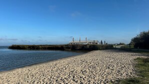A sandy beach with a building featuring a metal roof and tall, slender columns.
