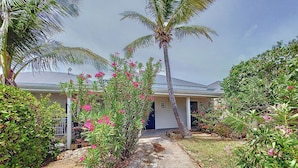 A pathway leading to a house with a white exterior and a dark roof, surrounded by lush greenery and flowering plants. - Seemingly unobstructed sea and marina view (Oyster Pond)