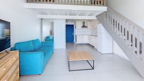 A spacious living area with a blue sofa, a wooden coffee table, a TV, and a kitchen in the background. - Seemingly unobstructed sea and marina view (Oyster Pond)