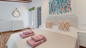 Een slaapkamer met een bed, kussens, een kaptafel, een schilderij en een raam.