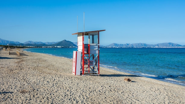 Una torre de socorrista en una playa con cielos despejados y montañas al fondo.