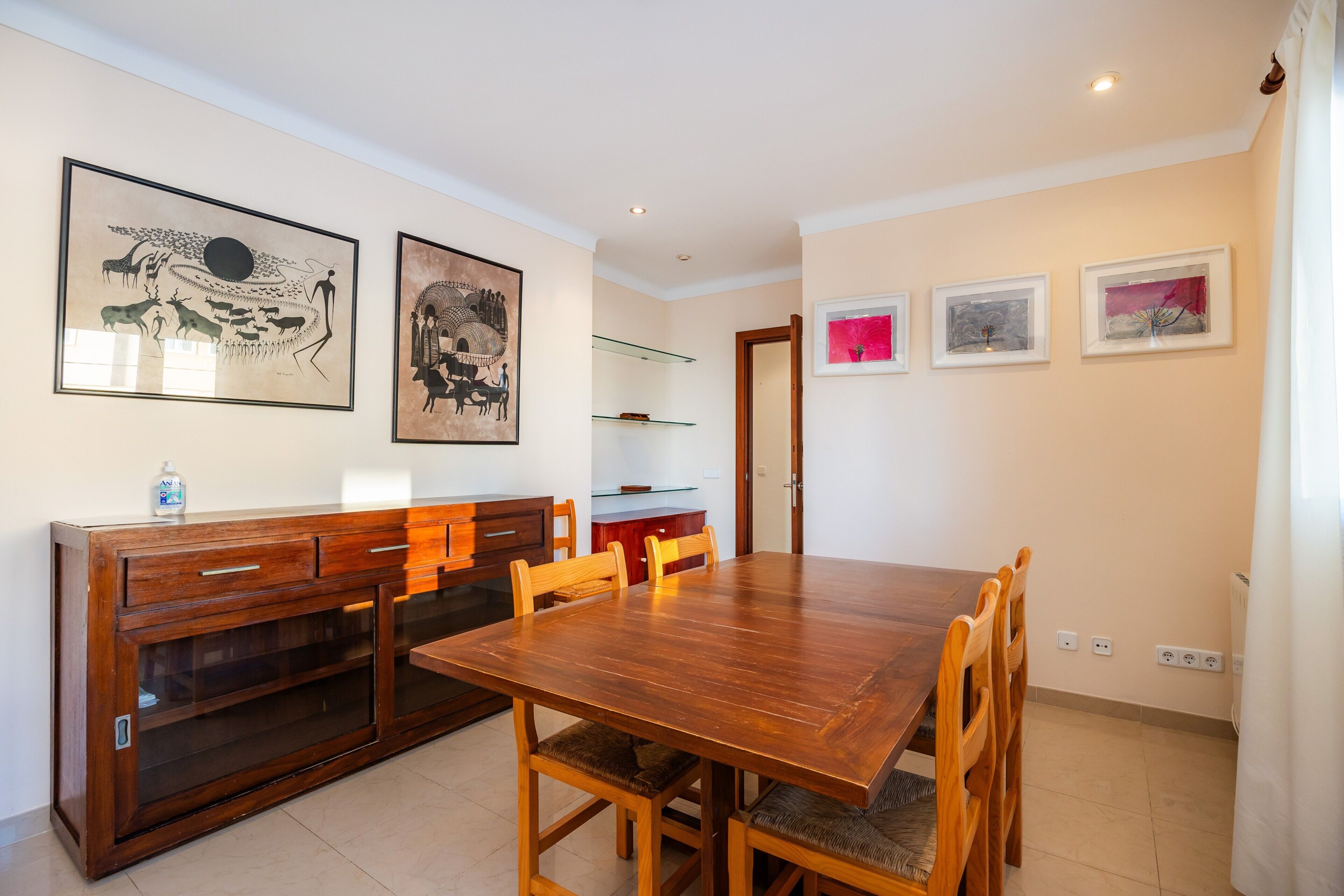 A dining area with a wooden table and chairs, a cabinet with drawers, and wall-mounted artwork.
