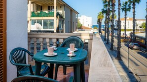 Un balcón con una mesa y sillas, con vista a una calle con palmeras y edificios.