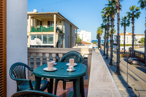 A balcony with a table and chairs, overlooking a street with palm trees and buildings.