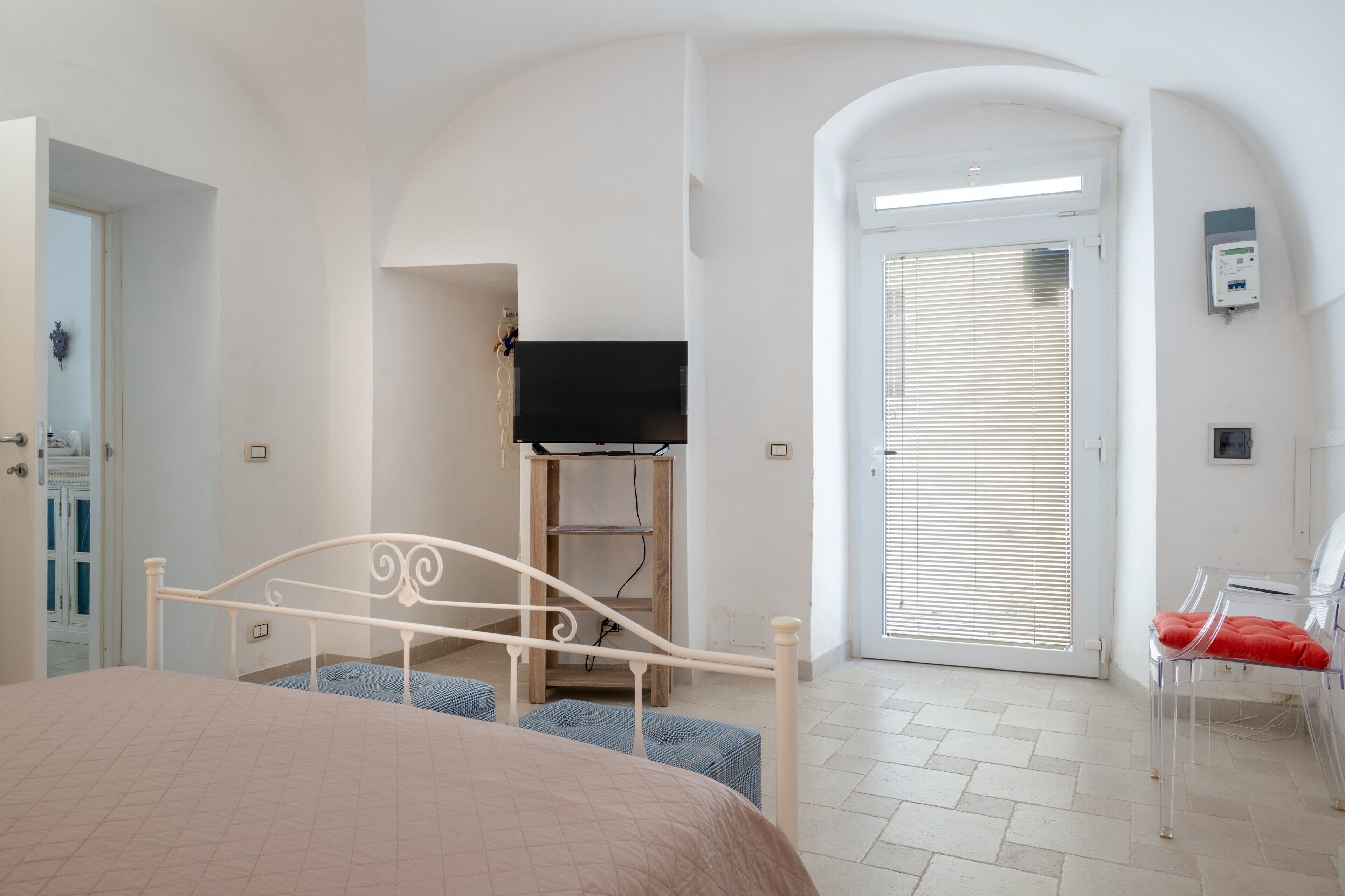 Un dormitorio con cama, televisor, una silla y una puerta con persianas.