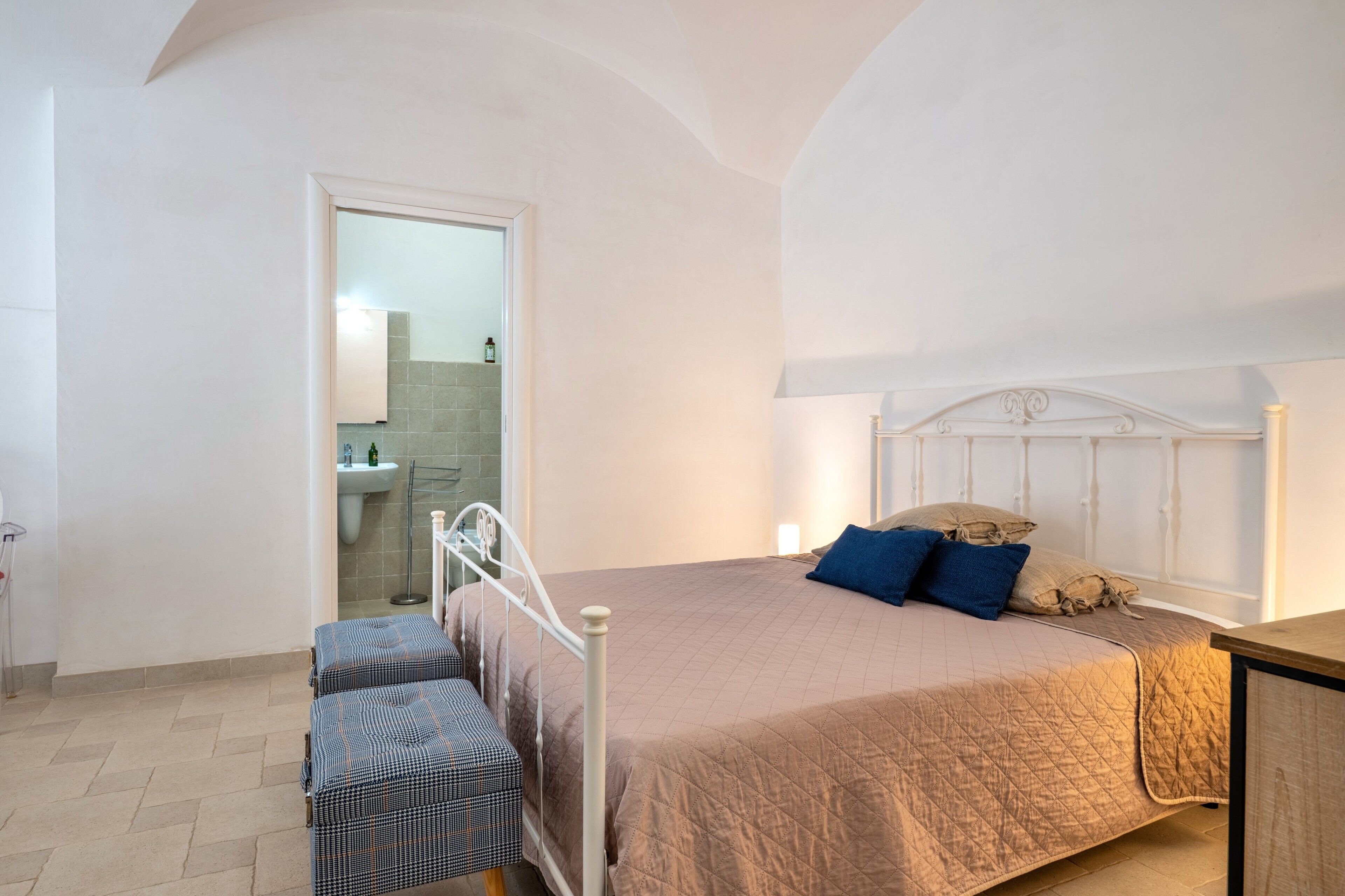Un dormitorio con cama, banco y vista al baño.