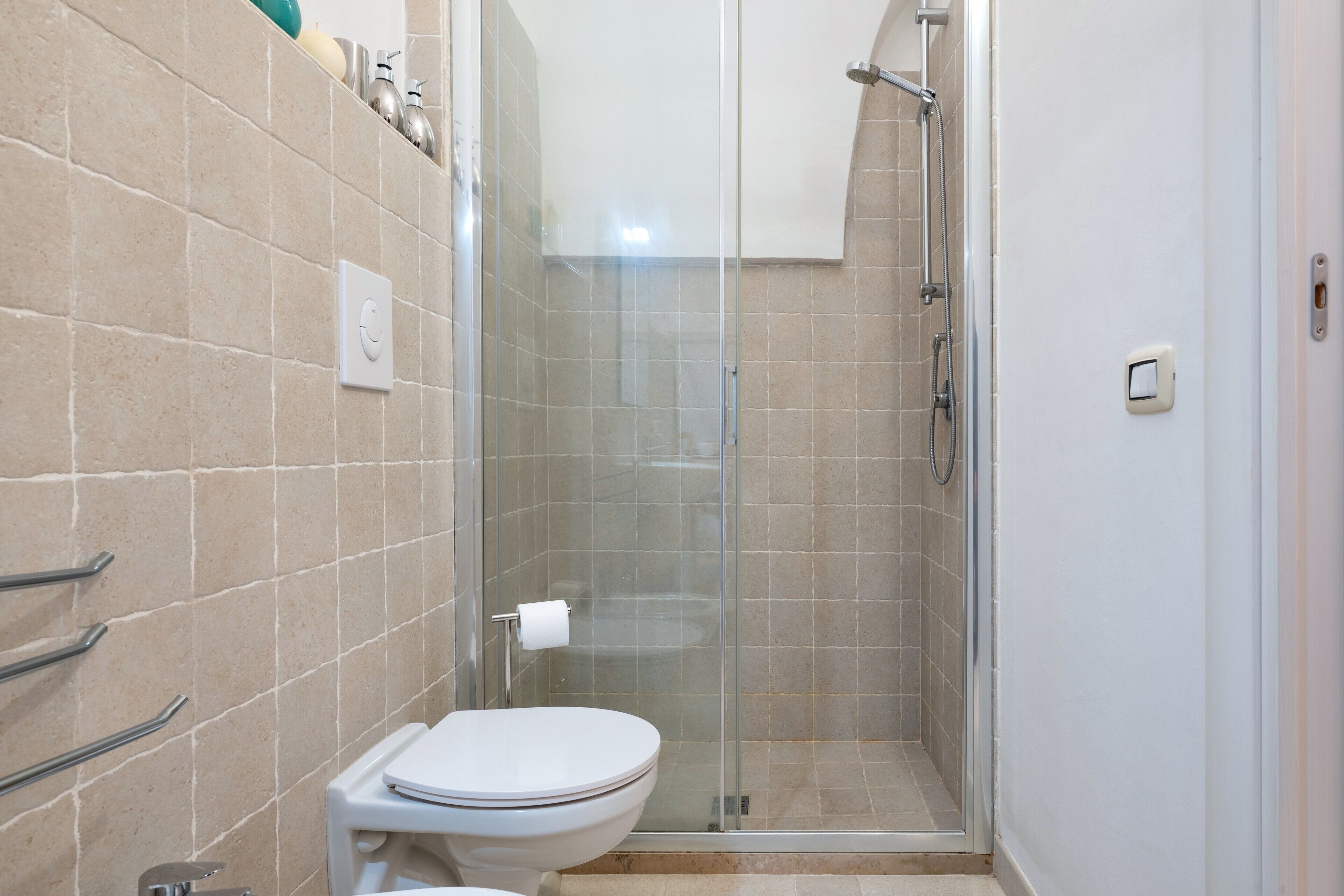 A bathroom with a toilet, a glass shower enclosure, and a tiled wall.