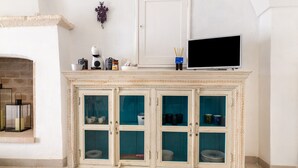 Een witte open haard met een bovenkant, een televisie erbovenop en een kast met glazen deuren eronder.