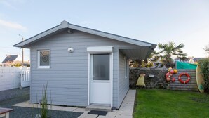 A small, single-story building with a door and window, surrounded by a grassy yard and a stone wall with a lifebuoy.