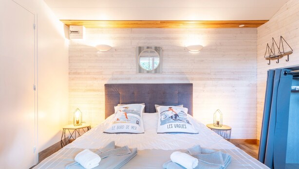 A double bed with two pillows, a headboard, a small round mirror, two bedside tables with lamps, and a wooden ceiling.
