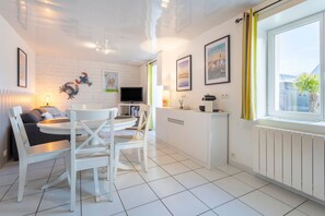 Een moderne keuken met witte kasten, een eethoek met witte stoelen, een flatscreen televisie en kunstwerken aan de muur.
