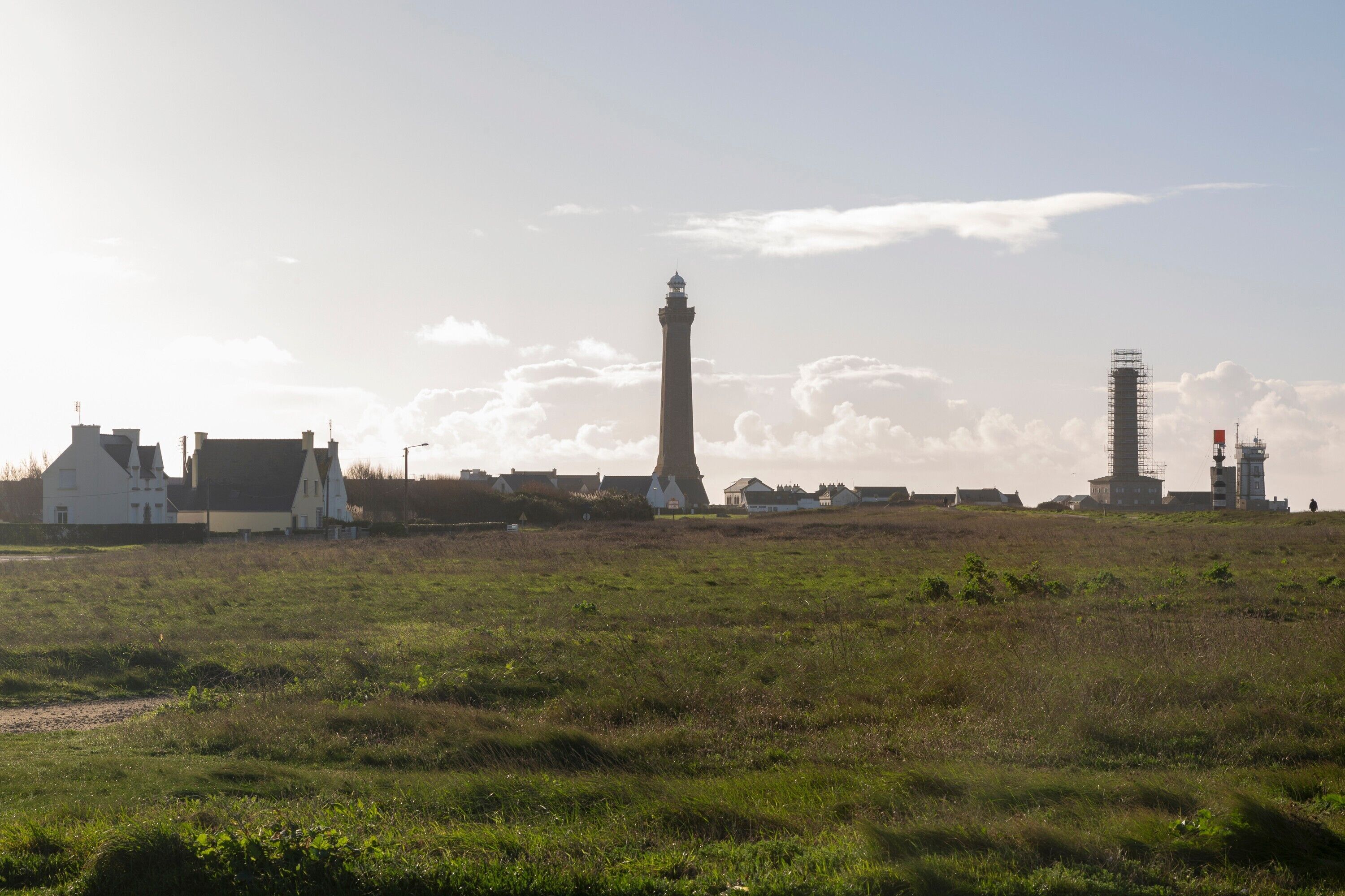 Un paisaje costero con un faro destacado, un edificio blanco y una obra en construcción.