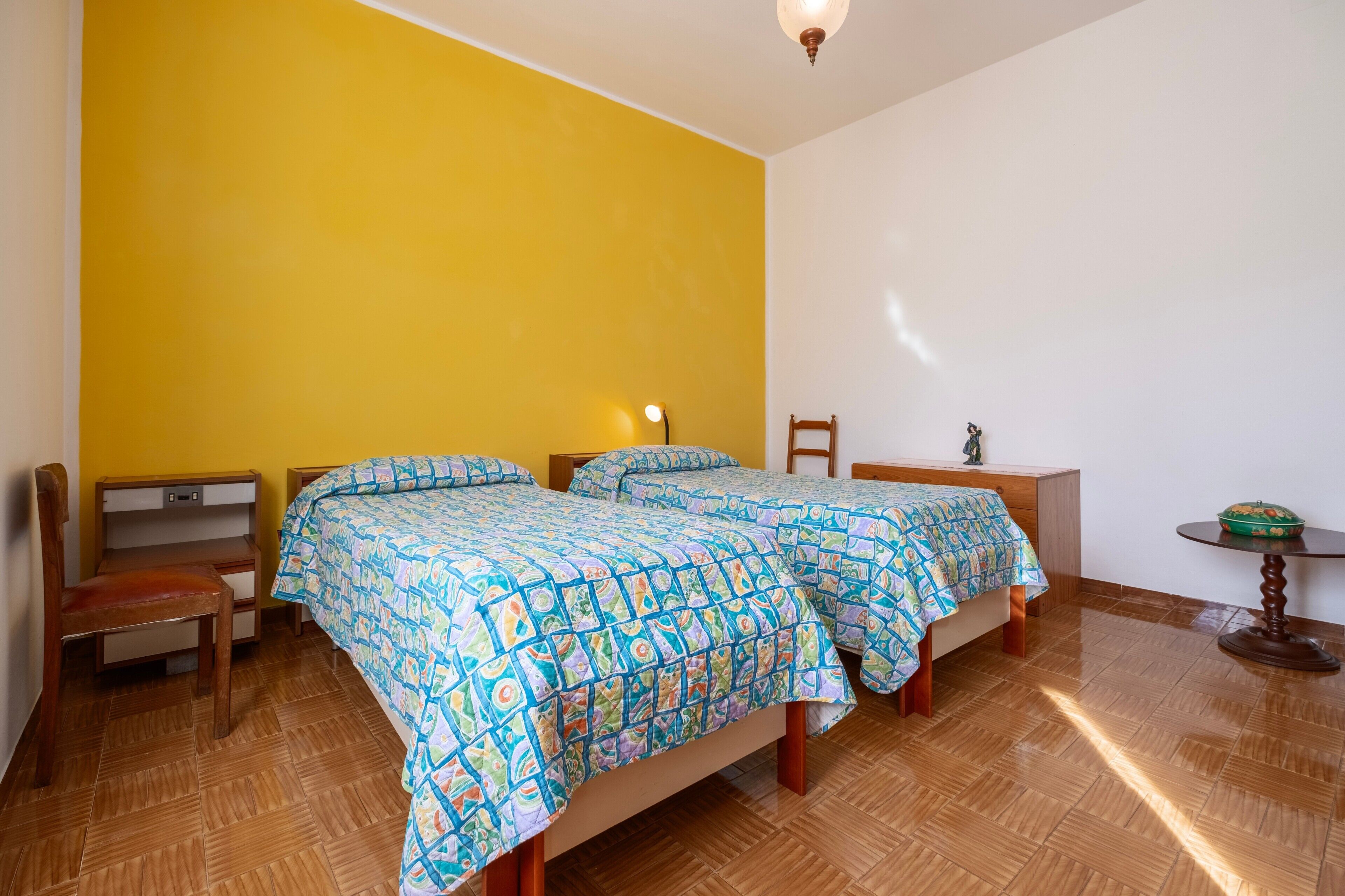 A room with two beds, a chair, a small table, and a lamp.