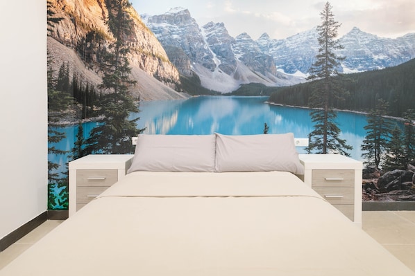 A bedroom with a bed, two bedside tables, and a large wall mural of a mountain lake.