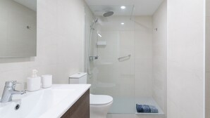 Une salle de bain moderne avec une douche à parois de verre, un lavabo blanc doté d’un distributeur de savon et des toilettes.