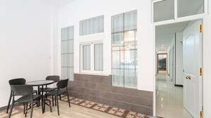 Une pièce avec un sol carrelé, une table ronde entourée de chaises et une porte donnant sur un autre espace.