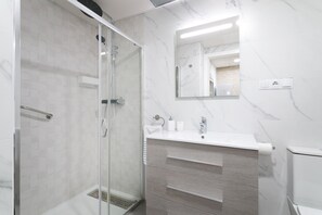 A modern bathroom with a glass-enclosed shower, a white sink with a marble countertop, and a large mirror.