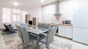 Une cuisine moderne avec une table à manger en verre, des chaises grises, une cuisinière encastrée et un four à micro-ondes.