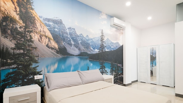 Une chambre avec une fresque murale représentant un paysage de montagne, un lit, une table de chevet et une armoire.