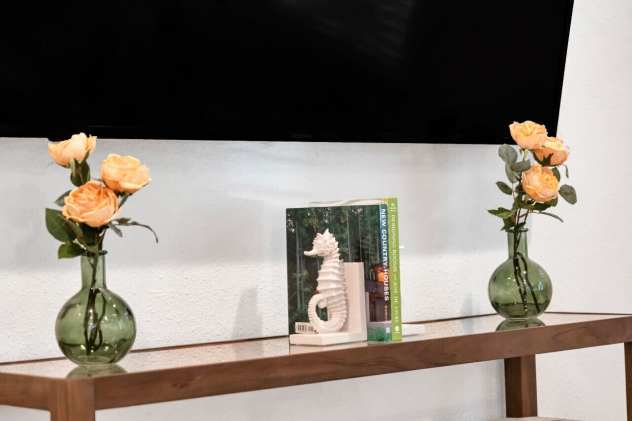 Dos jarrones con rosas sobre una estantería, un libro titulado 'New Country Houses' y una escultura de caballito de mar blanco.