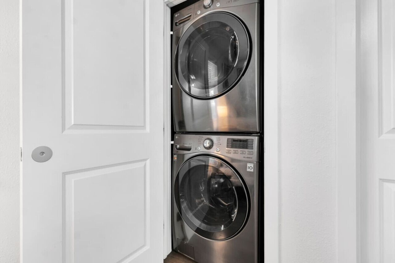 A compact, stainless steel front-loading washer and dryer unit installed in a white door frame.