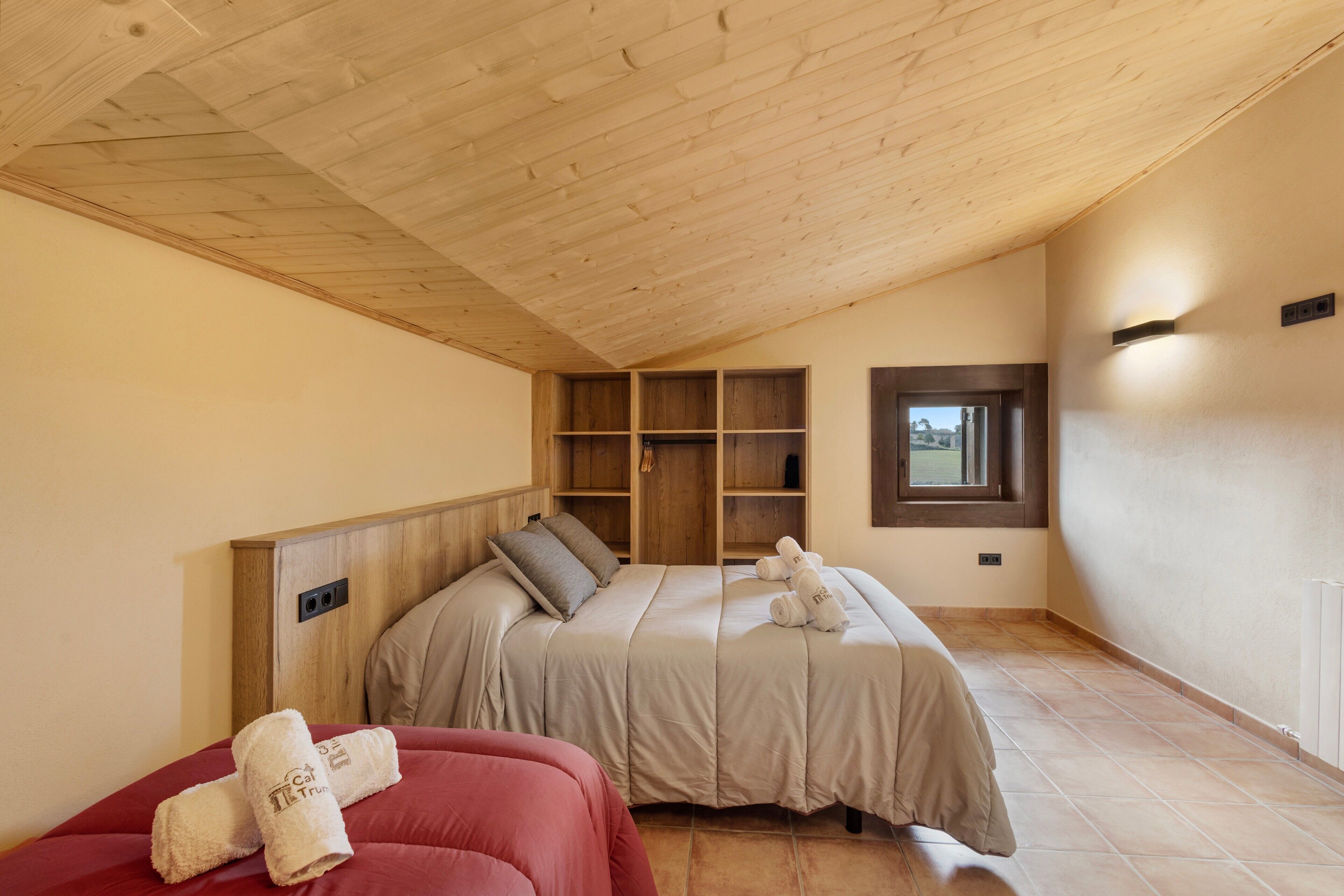 Une chambre avec un plafond en pente, un lit doté d’une tête de lit, une fenêtre et des étagères intégrées.
