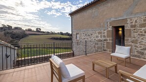 A balcony with a stone wall, two white cushioned chairs, a wooden table, and a view of a green landscape. - Rural Home 'Cal Trumfet' with Mountain View, Private Terrace and Wi-Fi (Casserres)