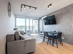 Un salon moderne comprenant un canapé, une table à manger, des chaises, un téléviseur fixé au mur et une grande fenêtre.