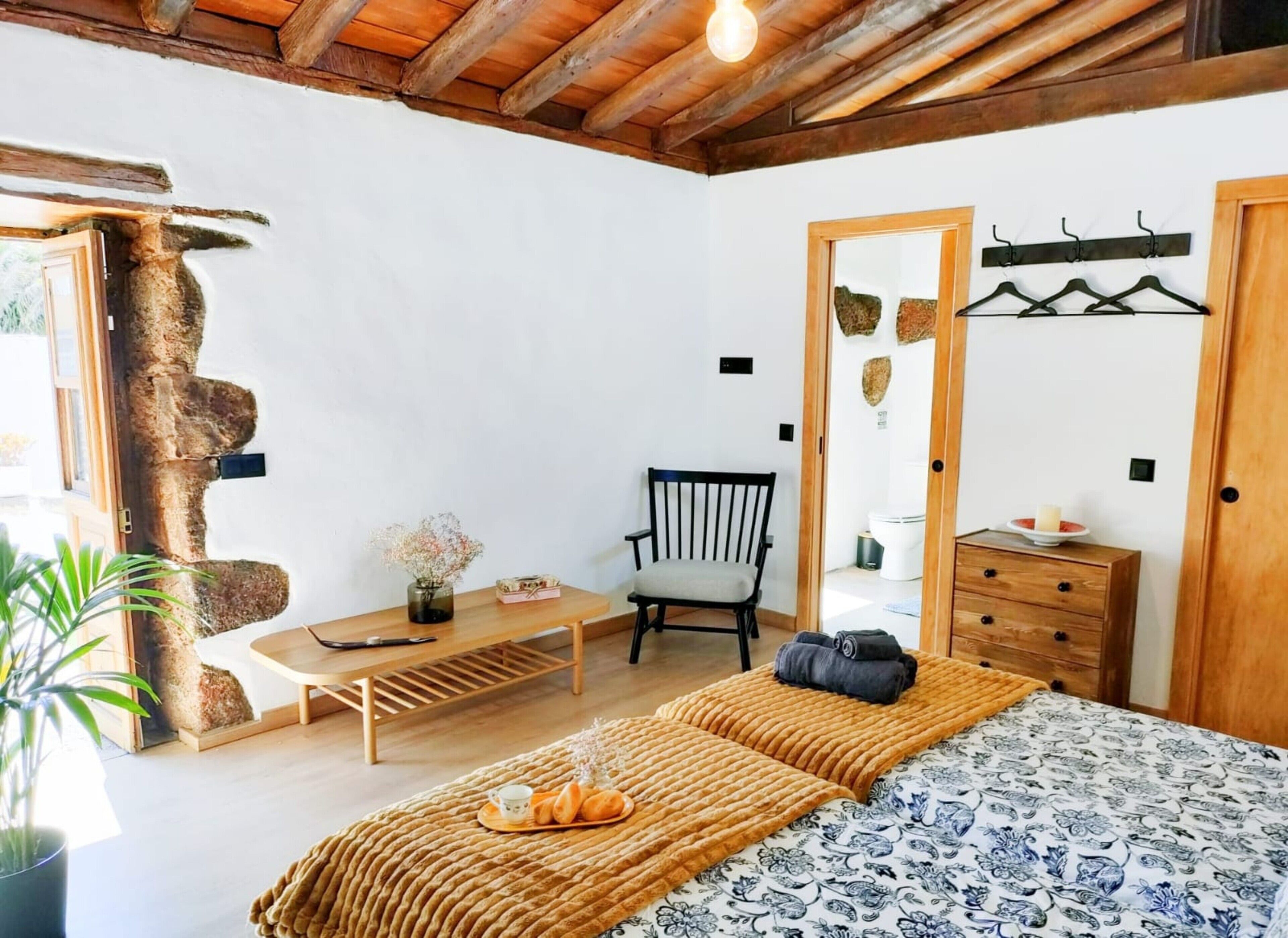 Een slaapkamer met een bed, een houten bankje, een stoel, een dressoir en een wandrek.
