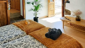 Una habitación con una cama, una planta en maceta, una mesa de madera y vistas a través de una puerta.