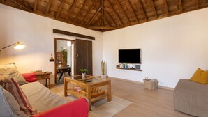 Una sala de estar con techo de madera, un televisor montado en la pared, un sofá, una mesa de centro y una lámpara.