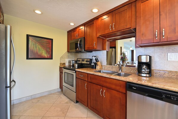 A modern kitchen with wooden cabinets, stainless steel appliances, and a granite countertop. - Castle at Hale Kama'oa (Naalehu)
