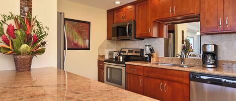 A kitchen with granite countertops, wooden cabinets, stainless steel appliances, and a decorative plant.