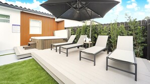 Un patio al aire libre con sillones, un jacuzzi y un paraguas grande.
