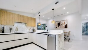 Una cocina moderna con encimeras de mármol blanco, armarios de madera y lavavajillas integrado.