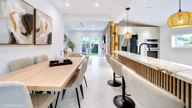 Una cocina moderna con una isla central, un comedor con una mesa larga y vistas al espacio de estar contiguo.