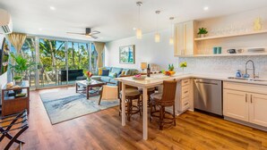 Una cocina moderna con zona de comedor, ventanas amplias y vista a palmeras.