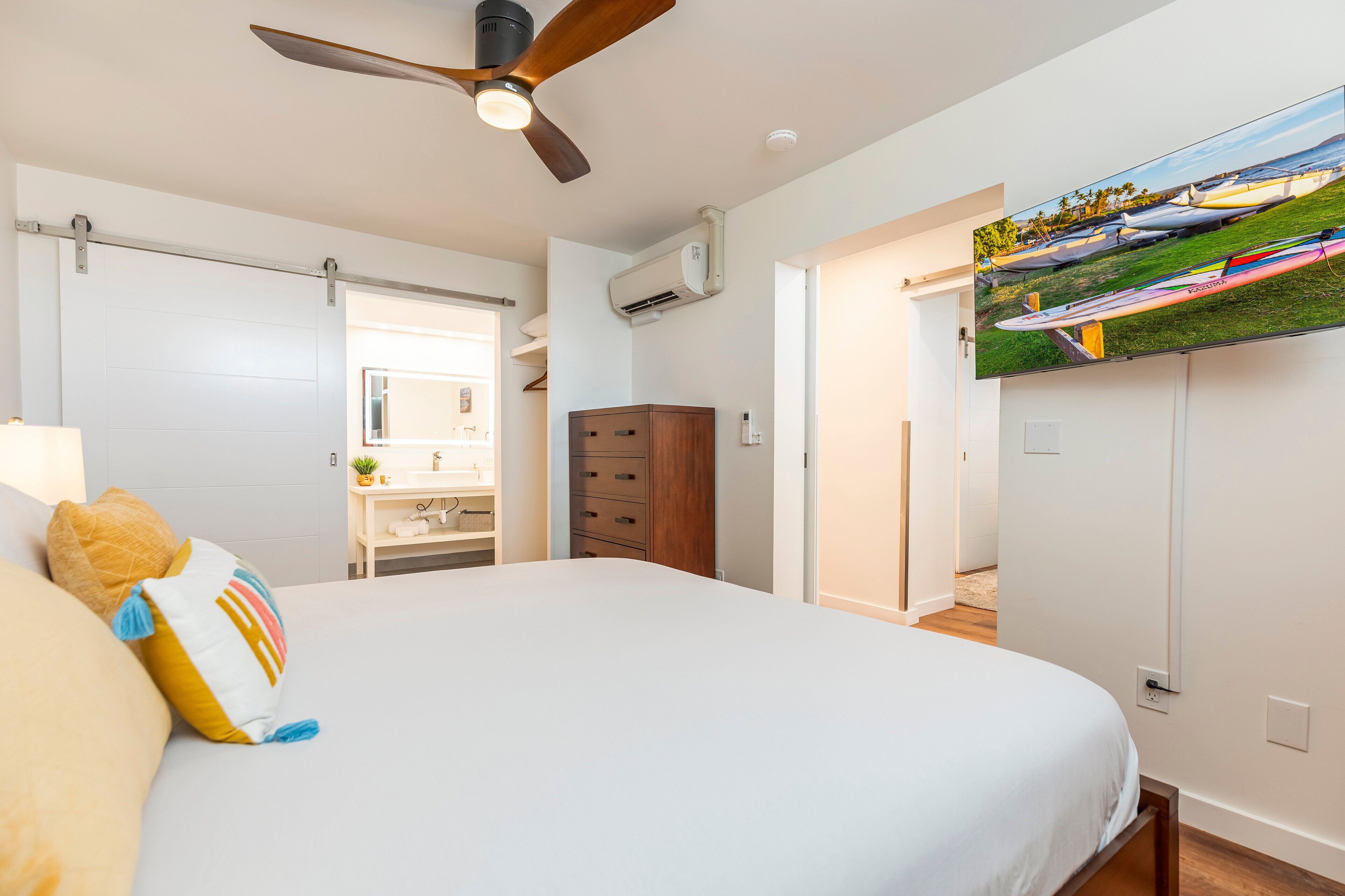 A bedroom with a bed, a ceiling fan, a TV, a wardrobe, and a bathroom visible through an open door.
