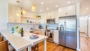 Una cocina moderna con armarios blancos, electrodomésticos de acero inoxidable y una isla central con taburetes de bar.