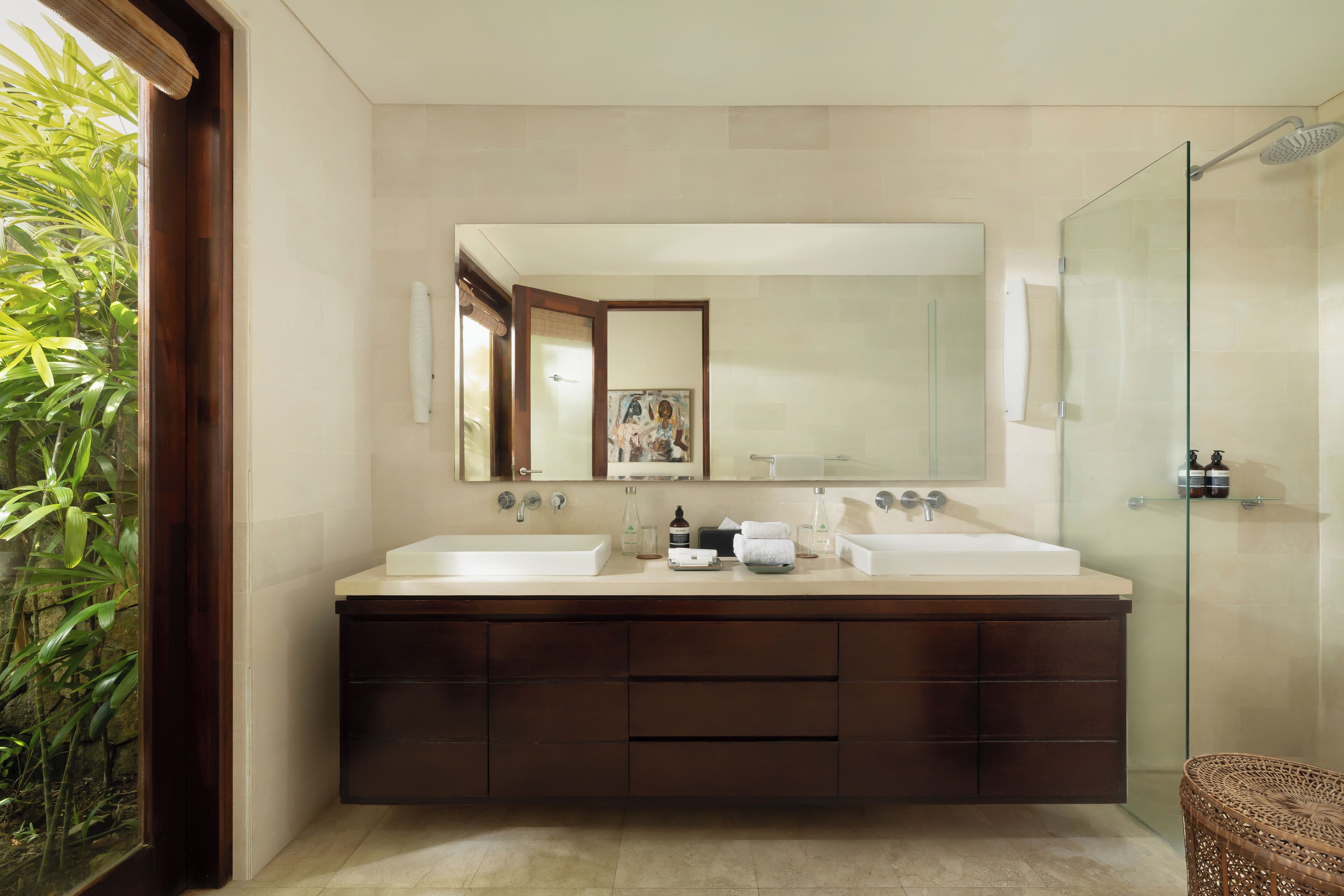 A modern bathroom with a large mirror, two sinks, dark wooden cabinets, and a glass shower enclosure.