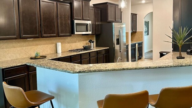 A modern kitchen with dark wood cabinets, a granite countertop, a stainless steel refrigerator, and a built-in island with bar seating. - Beautiful house in The Woodlands - Creekside (Tomball)